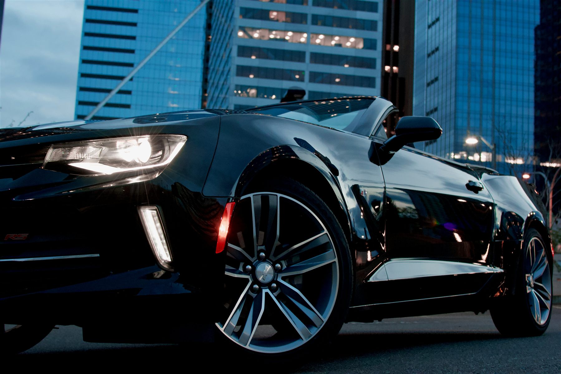 Carro convertible negro con las luces encendidas en una calle de la ciudad